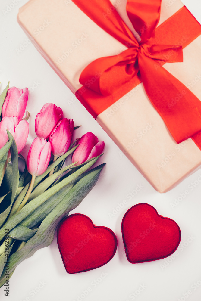 gift box with red heart. Bouquet of red tulips next to a gift with a red bow and 2 red hearts. Gift and flowers for Mother's Day or Valentine's Day. gift box with red heart. Bouquet of red tulips next to a gift with a red bow and 2 red hearts. Gift and flowers for Mother's Day or Valentine's Day.