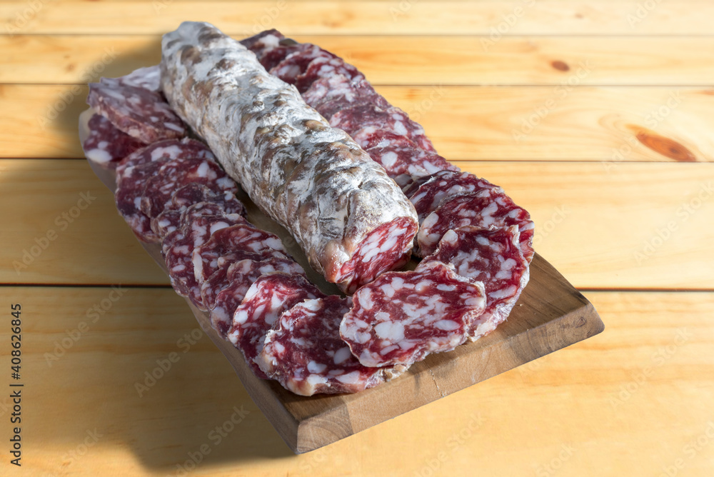 Salami Felino Italian, whole sausage with slices around on a wooden cutting board Salami Felino Italian, whole sausage with slices around on a wooden cutting board
