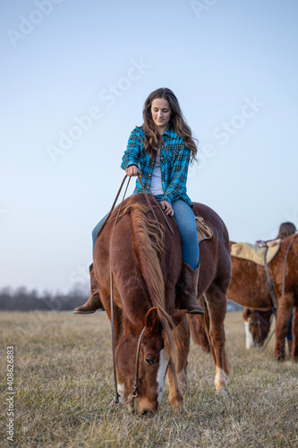 Cowgirl in Flannel Riding Grazing Horse