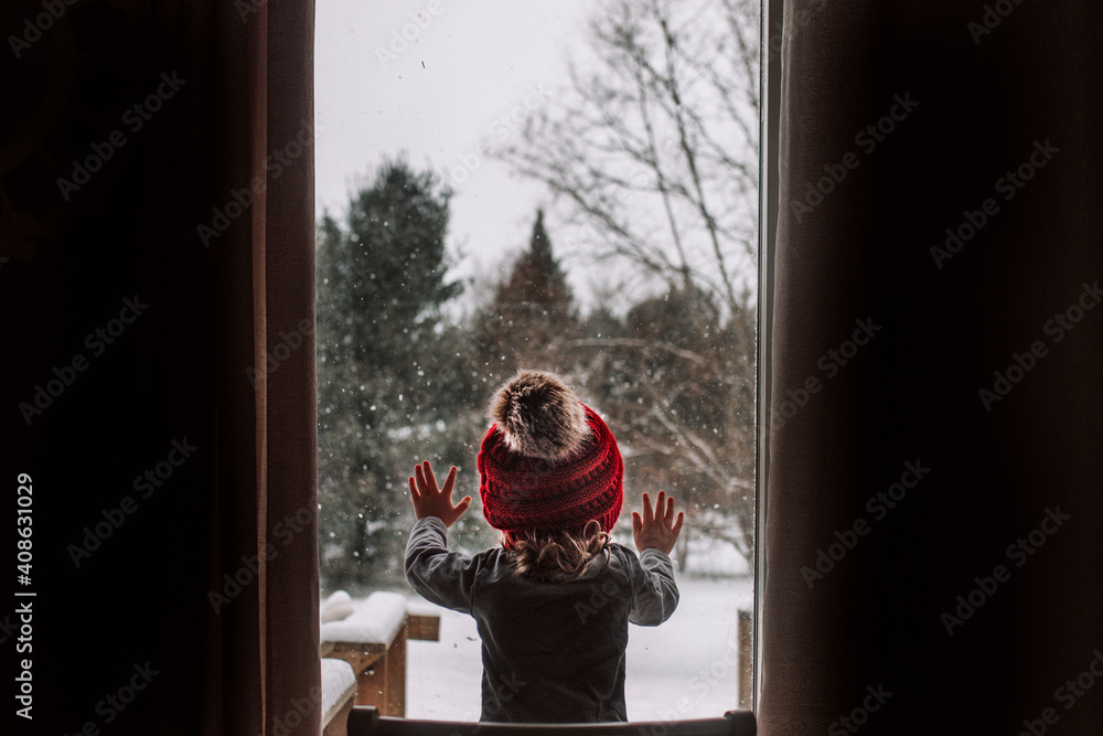 Little girl looks out the window during a snow day in the winter Little girl looks out the window during a snow day in the winter