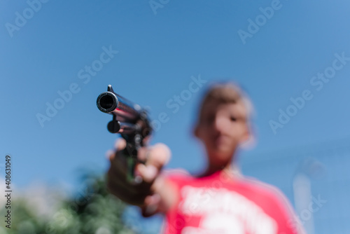 Blonde teenager wearing a red t - shirt pointing with a gun.
