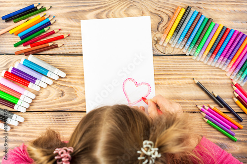 Little girl prepares cards with hearts for Valentine s Day. Drawing is done by a child with colored pencils or felt-tip pens. Children s drawing. View from above
