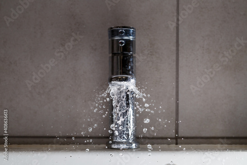 Broken water faucet in the bathroom sink. Water splashes from the silver faucet photo