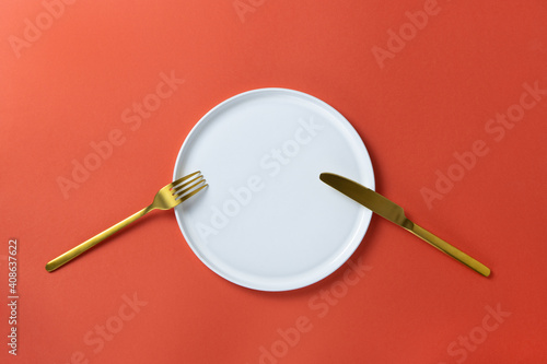 Fashionable blank white round plate with golden cutlery on red paper, minimal style flat lay, copy space. Mockup for restaurant, cafe, delivery service, social media. Concept Valentine's day food