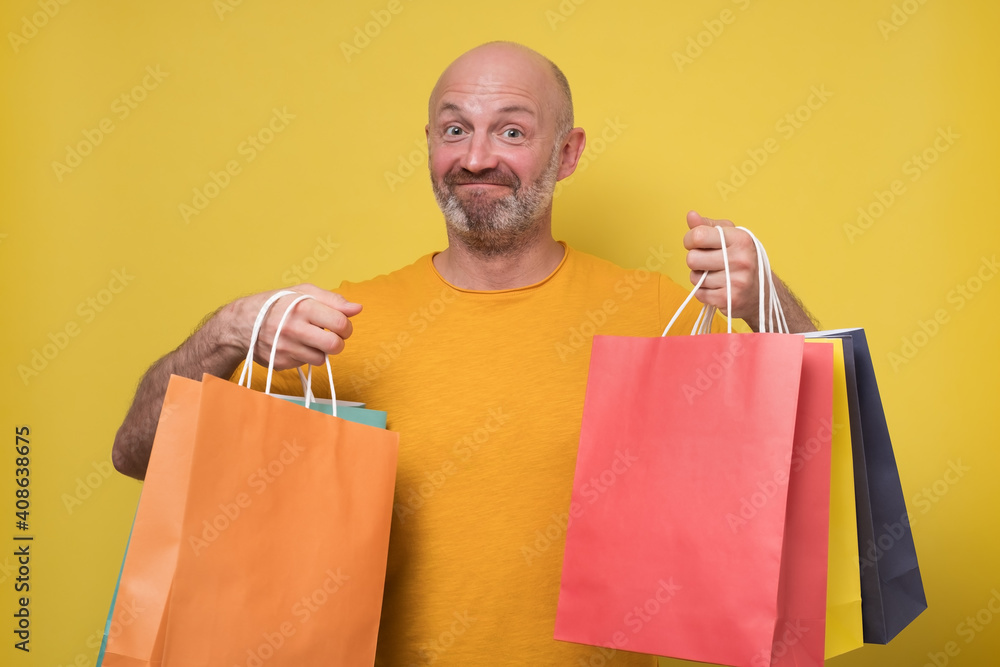 Mature caucasian man with packing bags after shopping. Studio shot on yellow wall. Mature caucasian man with packing bags after shopping. Studio shot on yellow wall.