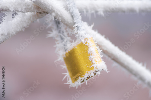 Frozen yellow padlock covered in frost during winter storm. Palencia, Spain.