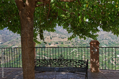 A Metal Railing on the edge of the pavement in the small Mountain Village of Sayalonga, with a cast Iron ornate seat for People to sit and admire the View.