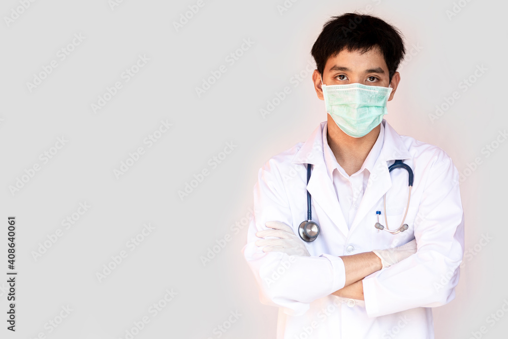 A doctor posing with arms crossed on a white background is wearing a medical face mask and stethoscope. Young Asian doctor wearing a white coat. A doctor posing with arms crossed on a white background is wearing a medical face mask and stethoscope. Young Asian doctor wearing a white coat.