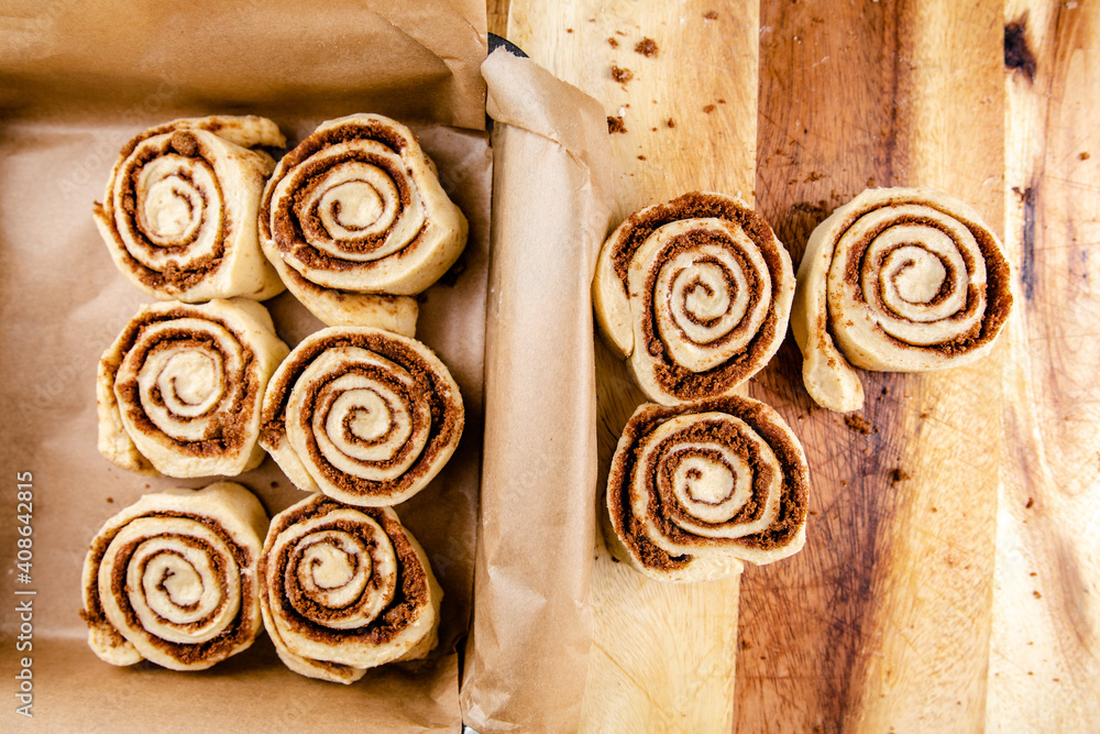 Cinnamon rolls laid on a table being put into a baking tray Cinnamon rolls laid on a table being put into a baking tray