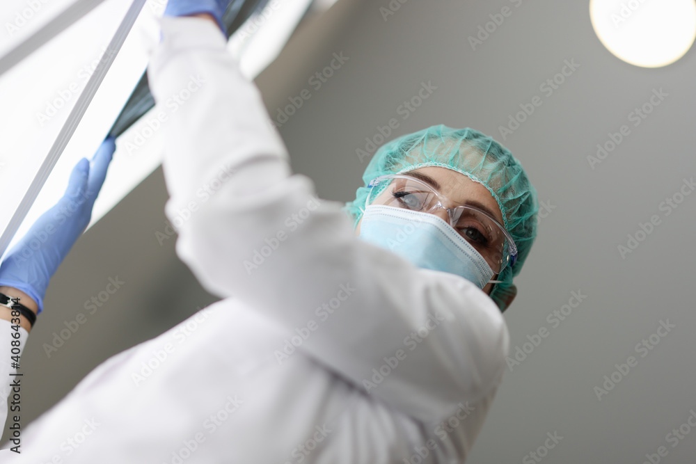 Naklejka premium Medic is holding an X-ray in medical protective mask. Doctors fight coronavirus infection concept