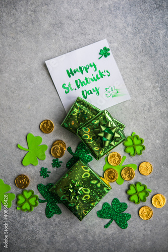 Decorative clover leaves, green gifts box, coins on stone background, flat lay. St. Patrick's Day celebration. Card Happy St. Patrick's Day