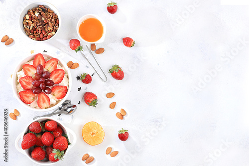Useful breakfast with ingredients, strawberry yogurt with muesli, grapes and honey on a bright table, fruit salad. Healthy and natural food concept, lifestyle, food for children, selective focus