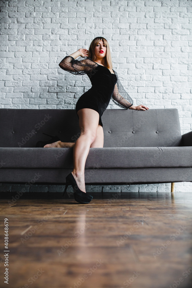 Fototapeta premium Young sexy blonde with naked legs in high heel shoes posing near the sofa