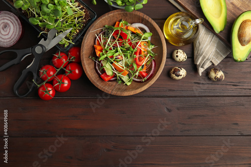 Salad with fresh organic microgreen in bowl on wooden table, flat lay. Space for text