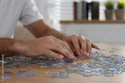 Man playing with puzzles at wooden table indoors, closeup