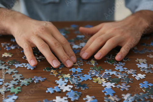 Man playing with puzzles at wooden table, closeup