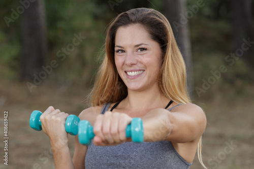 portrait of smiling beautiful woman exercising with dumbbell outdoors