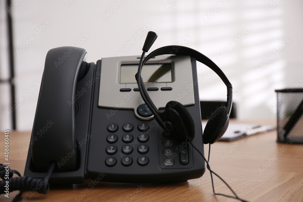 Desktop telephone and headset on wooden table in office. Hotline service Desktop telephone and headset on wooden table in office. Hotline service