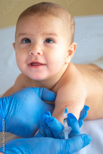 A doctor giving a vaccine to a baby in the hand. The child looks at the doctor and smiles. Vertical image