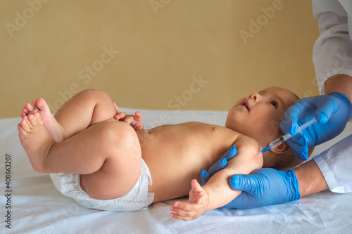 Pediatrician giving vaccine to baby lying on his back. The child looks at the doctor with interest