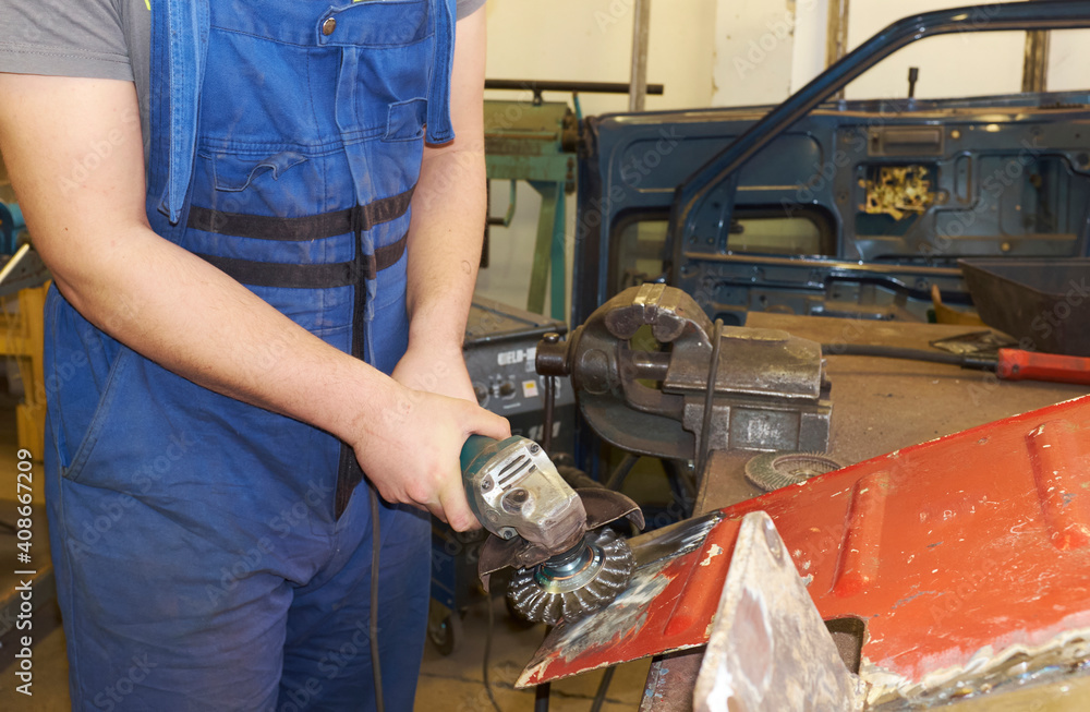 Car bodywork in a car repair workshop, man holding an angle grinder Car bodywork in a car repair workshop, man holding an angle grinder