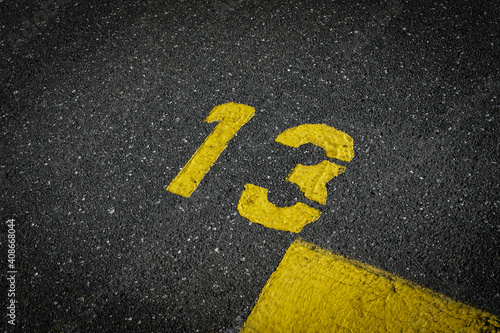 Grey asphalt road, yellow painted number thirteen on grey street, yellow lines like a corner on the road, space for text   © YK