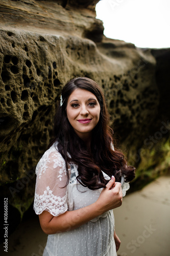 Newlywed Bride Standing Between Rocks on Beach in San Diego photo