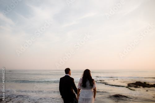 Newlyweds Standing on Rock at Beach in San Diego During Sunset photo