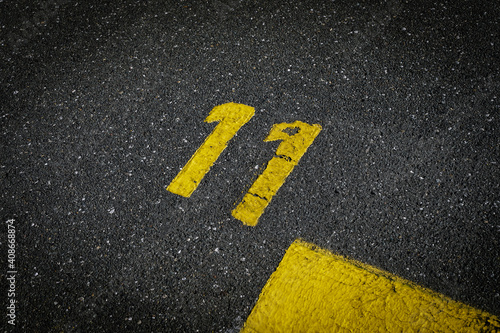 Grey asphalt road, yellow painted number eleven on grey street, yellow lines like a corner on the road, space for text 