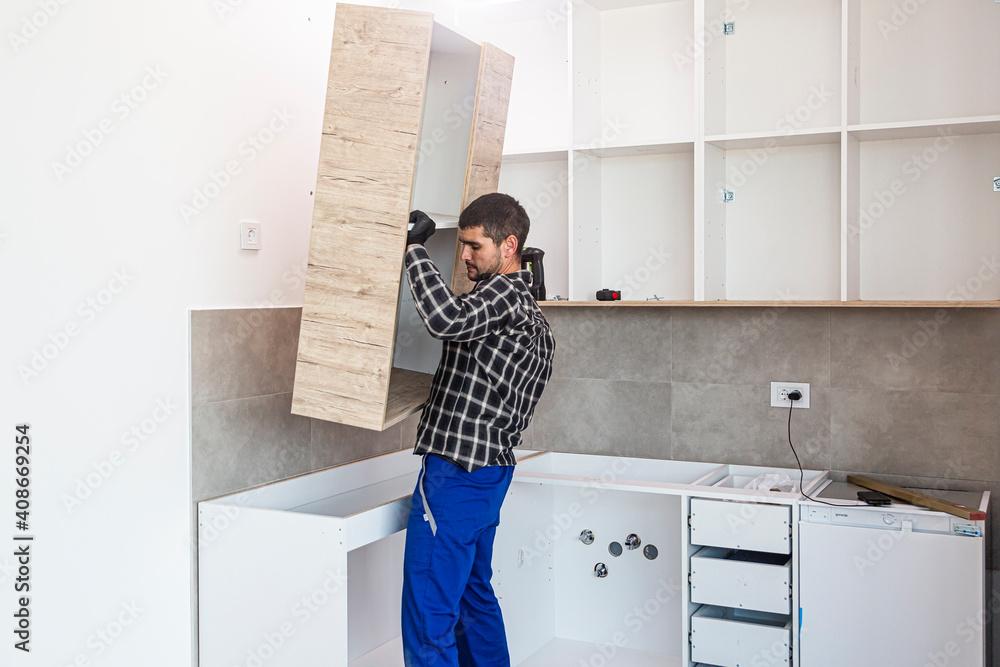 The carpenter places the newly assembled kitchen shelves in the intended place. The carpenter places the newly assembled kitchen shelves in the intended place.