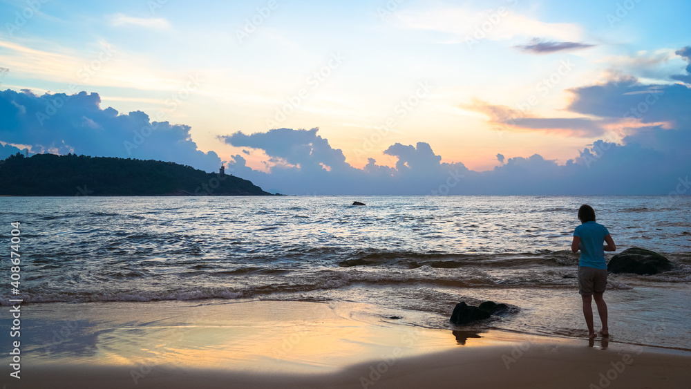Fototapeta premium A woman is walking on the beach during the sunrise blue hours, travel and freedom concept, morning walk along the sea