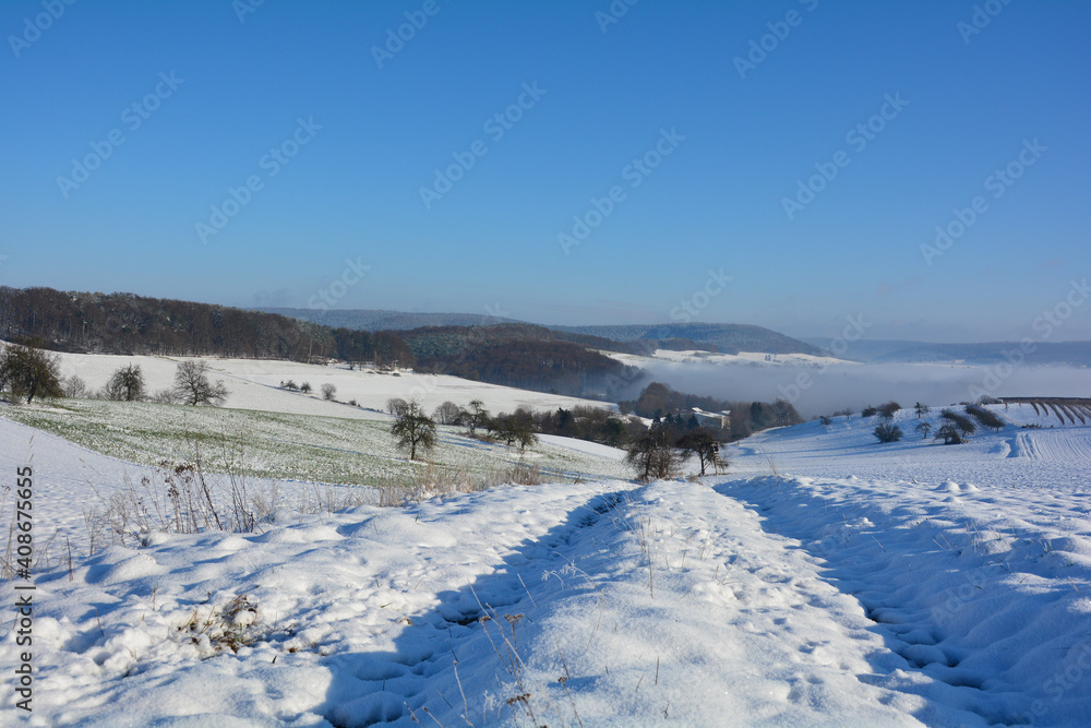 Winter landscape with fields and fog in the valley, with snow and a blue sky