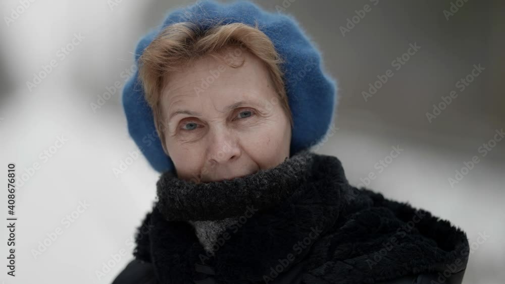 Portrait of an elderly woman in winter clothes, standing outdoors in a park in winter, looking at the camera. The concept of people. Portrait of an elderly woman in winter clothes, standing outdoors in a park in winter, looking at the camera. The concept of people.