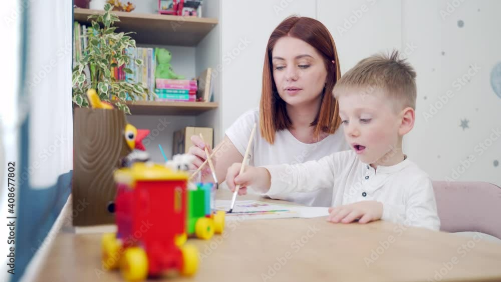 Happy family. Mom and pretty cute son are drawing at leisure at home sitting a table. Mother and preschool child spend time together. Motherhood. hobby and favorite pastime of parents in the nursery Happy family. Mom and pretty cute son are drawing at leisure at home sitting a table. Mother and preschool child spend time together. Motherhood. hobby and favorite pastime of parents in the nursery