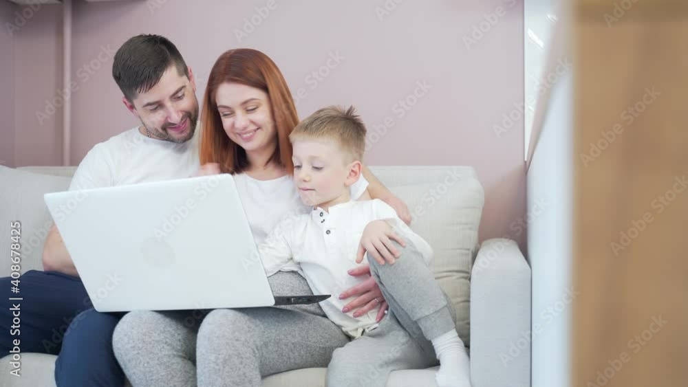 young happy family dad and mom with young children communicates online on laptop remotely. Waving hands and laughing sitting on the couch in the living room or kitchen at home talking to grandparents young happy family dad and mom with young children communicates online on laptop remotely. Waving hands and laughing sitting on the couch in the living room or kitchen at home talking to grandparents