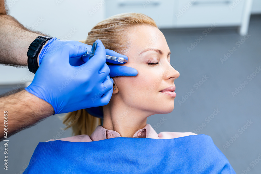 Attractive woman is getting a rejuvenating facial injections. She is sitting calmly at clinic. The expert beautician is filling female wrinkles by hyaluronic acid. Attractive woman is getting a rejuvenating facial injections. She is sitting calmly at clinic. The expert beautician is filling female wrinkles by hyaluronic acid.