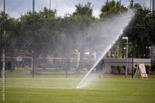 Sprinkler on a ball field at a park, with a sign saying "Field Closed for turf re growth and maintenance".
