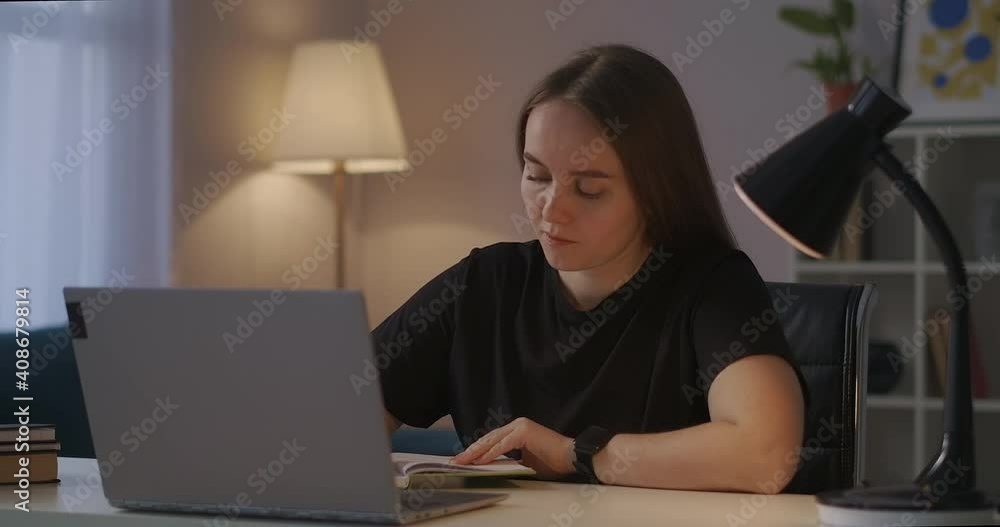 woman is making notes in notebook and viewing learning video tutorial on screen of laptop, studying online at home at evening woman is making notes in notebook and viewing learning video tutorial on screen of laptop, studying online at home at evening