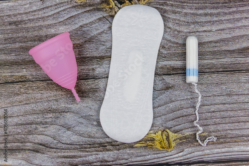 Sanitary pad, tampons and menstrual cup on wooden background. Top view. Concept of critical days, menstruation, feminine hygiene
