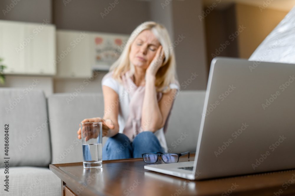 Sad or sick caucasian middle aged defocused female freelancer, suffering from headache, tired of working overtime online, sitting at home in the living room, with closed eyes, need a rest Sad or sick caucasian middle aged defocused female freelancer, suffering from headache, tired of working overtime online, sitting at home in the living room, with closed eyes, need a rest