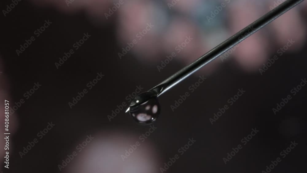 Syringe needle with a drop of serum on top. Blurred background that is reflected in the serum drop. Syringe needle with a drop of serum on top. Blurred background that is reflected in the serum drop.