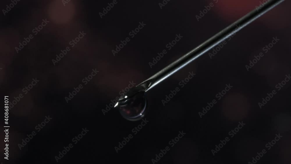 Syringe needle with a drop of serum on top. Blurred background that is reflected in the serum drop. Syringe needle with a drop of serum on top. Blurred background that is reflected in the serum drop.