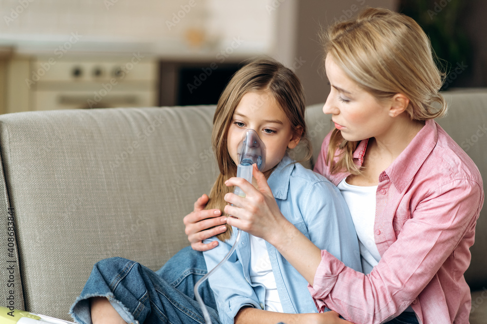 A caring sad mother makes inhalations using inhaler to her beloved little sick upset daughter. The child fell ill with the flu, cough, runny nose