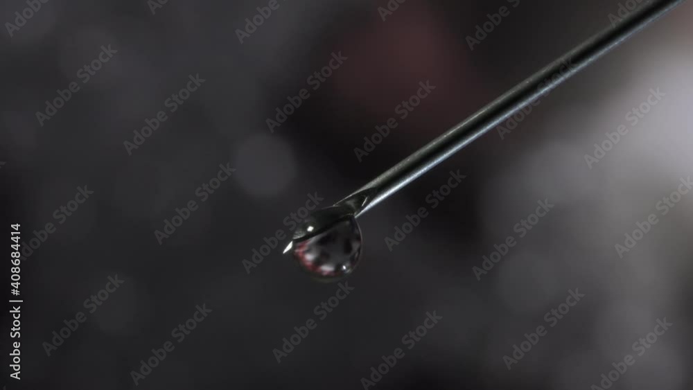 Syringe needle with a drop of serum on top. Blurred background that is reflected in the serum drop. Syringe needle with a drop of serum on top. Blurred background that is reflected in the serum drop.
