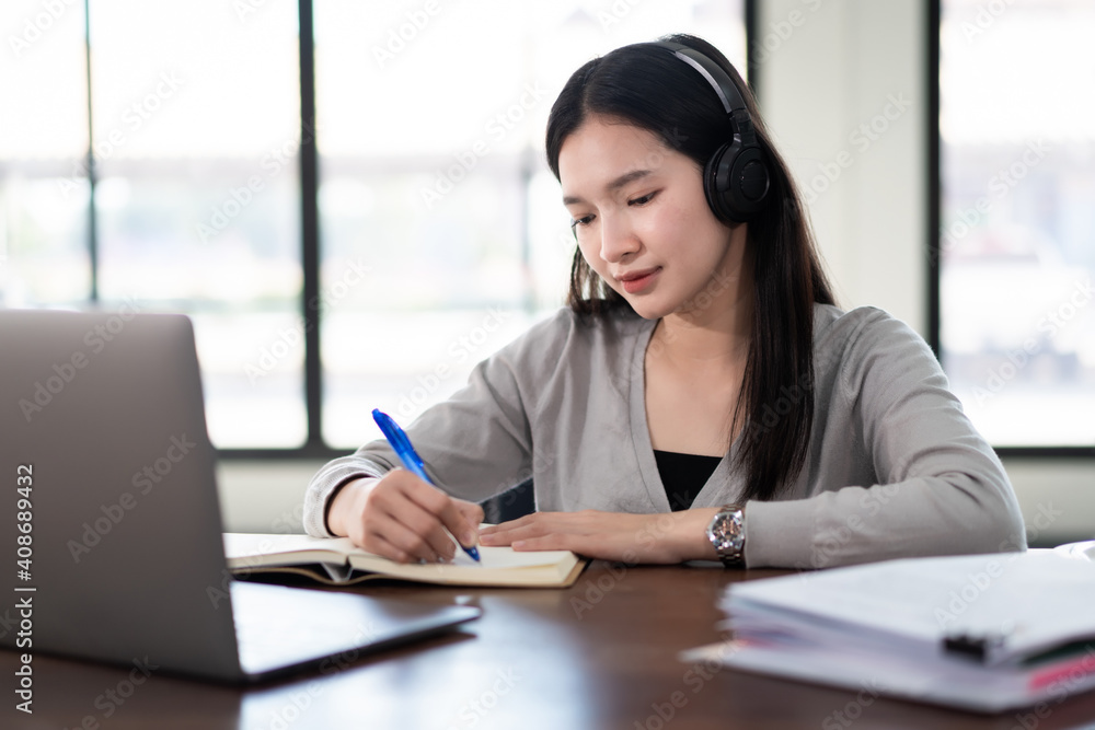 Young asian girl student wears wireless headphones write on the notebook to study language online watch and listen to the lecturer, webinar via video call e-learning at home, distance education Young asian girl student wears wireless headphones write on the notebook to study language online watch and listen to the lecturer, webinar via video call e-learning at home, distance education