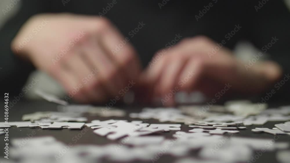 Puzzle pices falling on a dark table and bouncing off with a person's hands trying to solve the puzzle in the background. Shot in 4K, Slow Motion with Shallow Depth of Field. Puzzle pices falling on a dark table and bouncing off with a person's hands trying to solve the puzzle in the background. Shot in 4K, Slow Motion with Shallow Depth of Field.