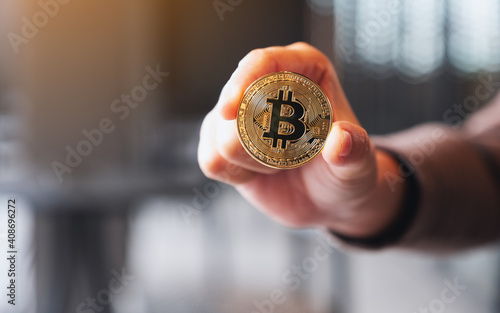 Closeup image of a hand holding and showing a gold colour bitcoin