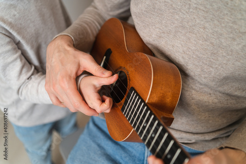 Dad teaches his daughter to play the ukulele. Home teaching to play the guitar. Close up of ukulele strings and hands