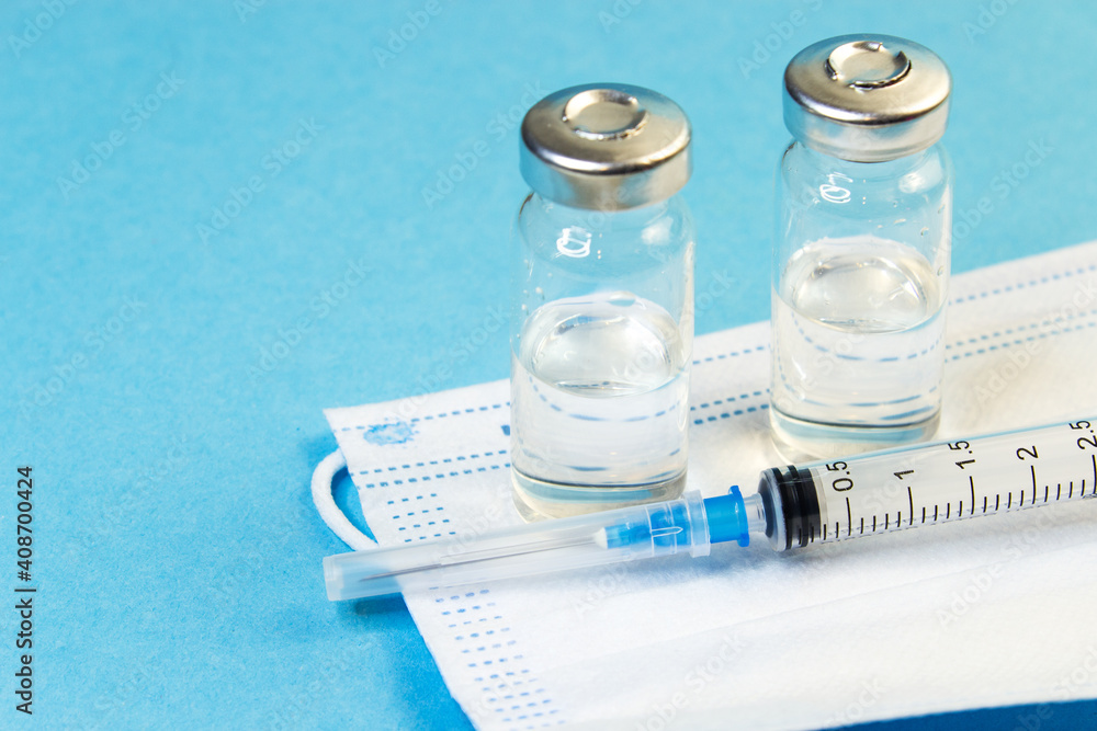 Vaccination against viruses. COVID 19 coronavirus vaccine. Glass bottle with injection solution, syringe and medical mask. Copy space. Vaccination against viruses. COVID 19 coronavirus vaccine. Glass bottle with injection solution, syringe and medical mask. Copy space.