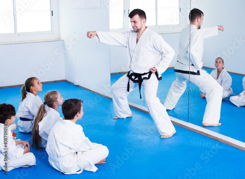 Young man training new karate moves with kids during class